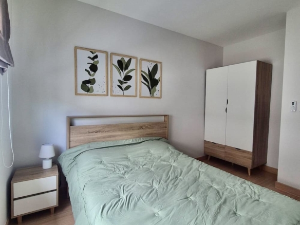 Bedroom with a wooden bed, mint green quilt, and matching nightstand lamp on the left; wardrobe on the right; three botanical prints above the headboard.