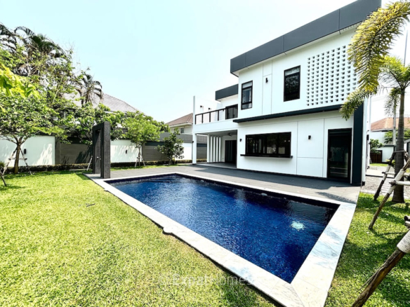 Modern white two-story house with a rectangular blue pool in the foreground and a green lawn.