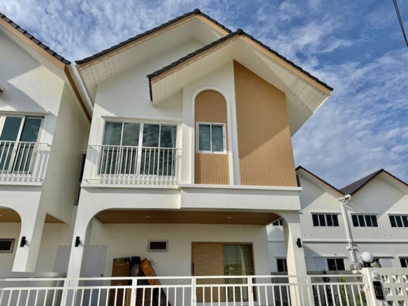 Front view of a white two-story townhouse with a balcony, arched window and vertical wood panel accent, gated entrance under a blue sky.
