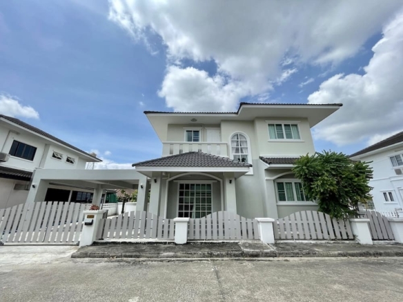 Two-story white house with a white picket fence and a small front yard under a blue sky split by clouds.