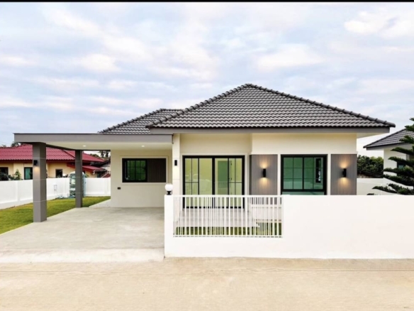Modern single-story house with a tiled gray roof, white exterior, long driveway, and a small front gate.