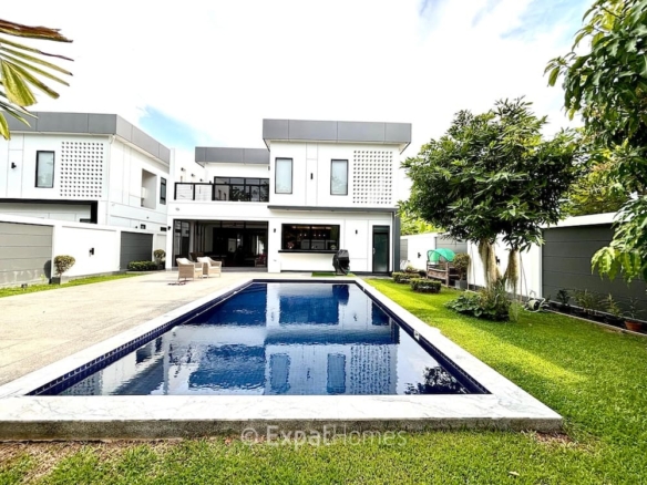 Modern two-story white house with a rectangular in-ground pool in the backyard, surrounded by a green lawn and patio seating area B.