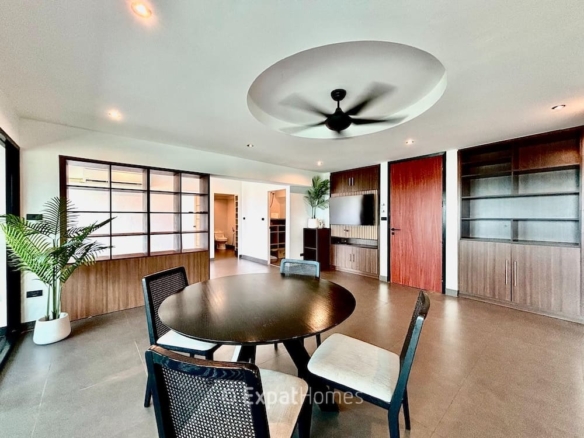 Modern dining room with a round dark wood table and four chairs, a large ceiling fan, built-in cabinets, and a potted plant in a bright, open space.