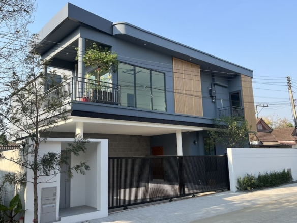 Modern two-story gray house with glass balcony and front gate on a sunny street