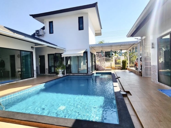 Modern backyard with a rectangular pool, glass doors, and a white house on a sunny day.