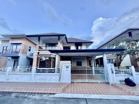 Two-story modern house with a gated driveway and tiled front path, flanked by neighboring homes under a blue sky.|Concise front view of a contemporary home with a white fence, metal gate, and a covered carport.|Front facade of a beige-and-white two-story house with brown pillars and a gated entrance.