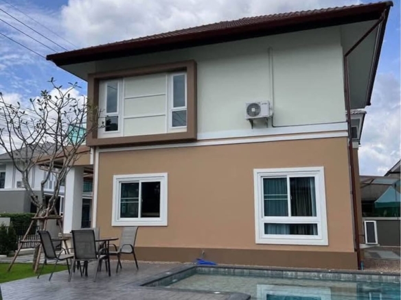 Two-story modern house with beige and white siding, pool in the foreground and outdoor seating on a tiled patio.