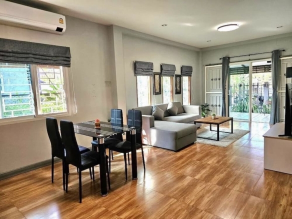 Open-concept living room with a glass dining table and black upholstered chairs, gray sofa, and a wooden floor