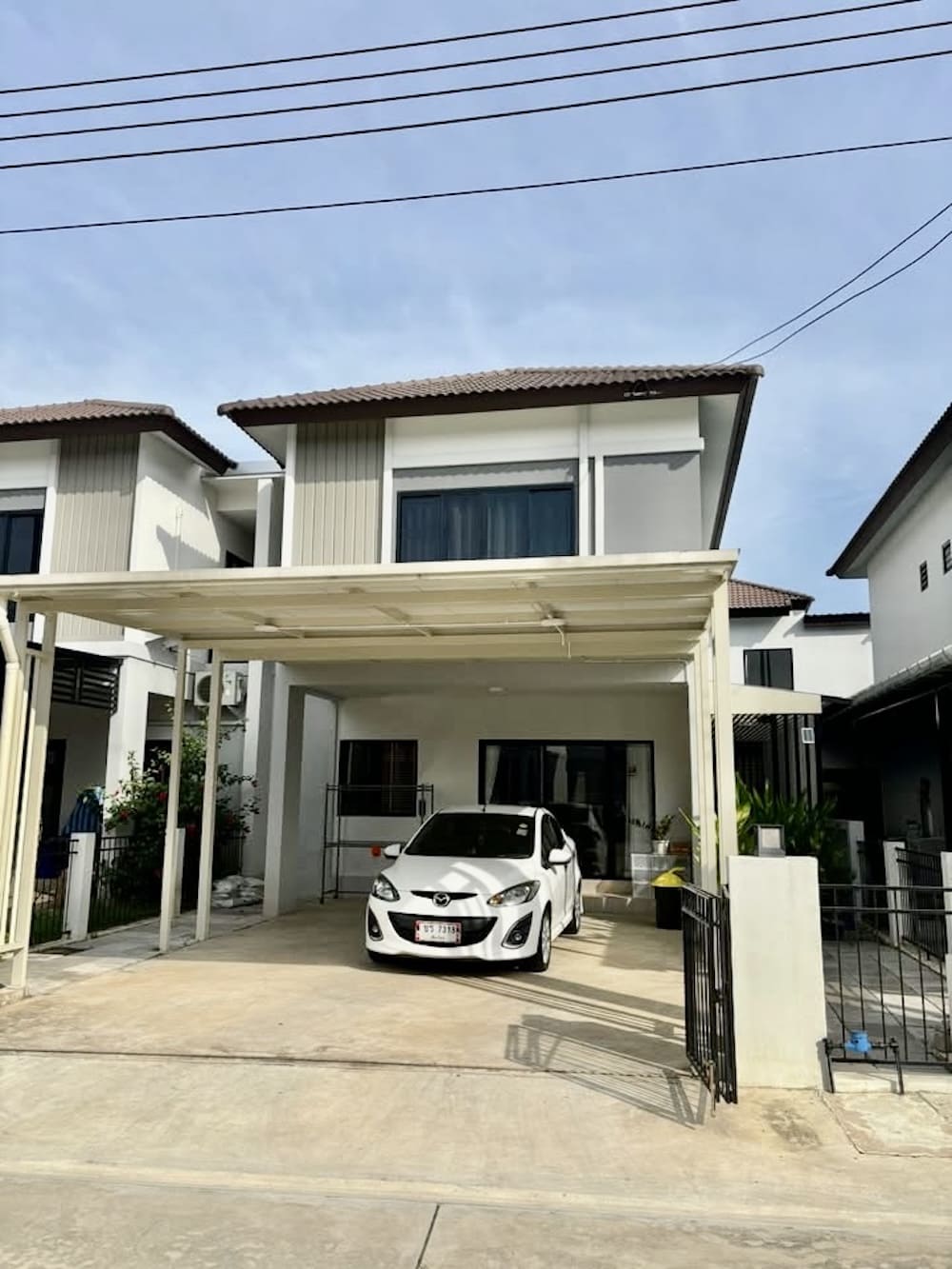 White sedan parked under a covered driveway in front of a modern two-story house with beige and gray exterior.