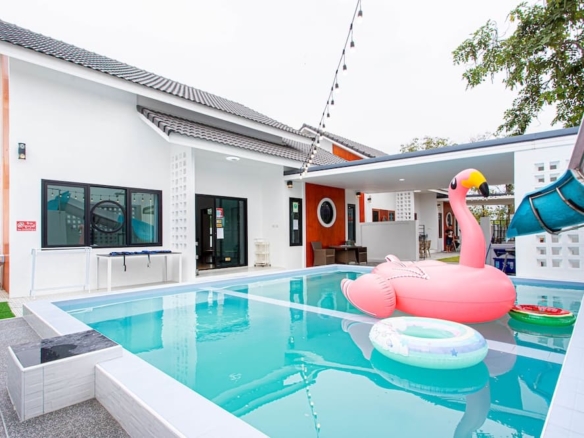 Modern villa with a rectangular pool, pink flamingo float, and string lights across an outdoor patio area