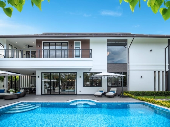 Modern two-story white house with a large backyard pool and outdoor seating under umbrellas.
