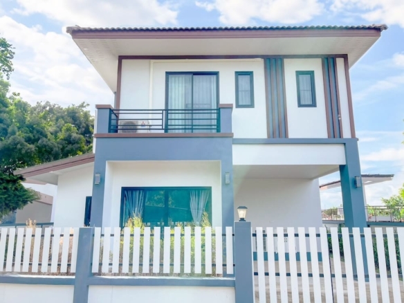 Two-story modern house with white/gray exterior, balcony on second floor, and a white picket fence.