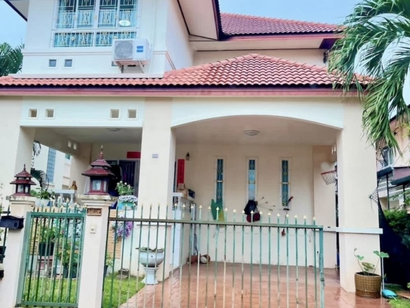 Two-story cream house with red tile roof, gated pink-tiled front yard, and potted plants near the entrance.