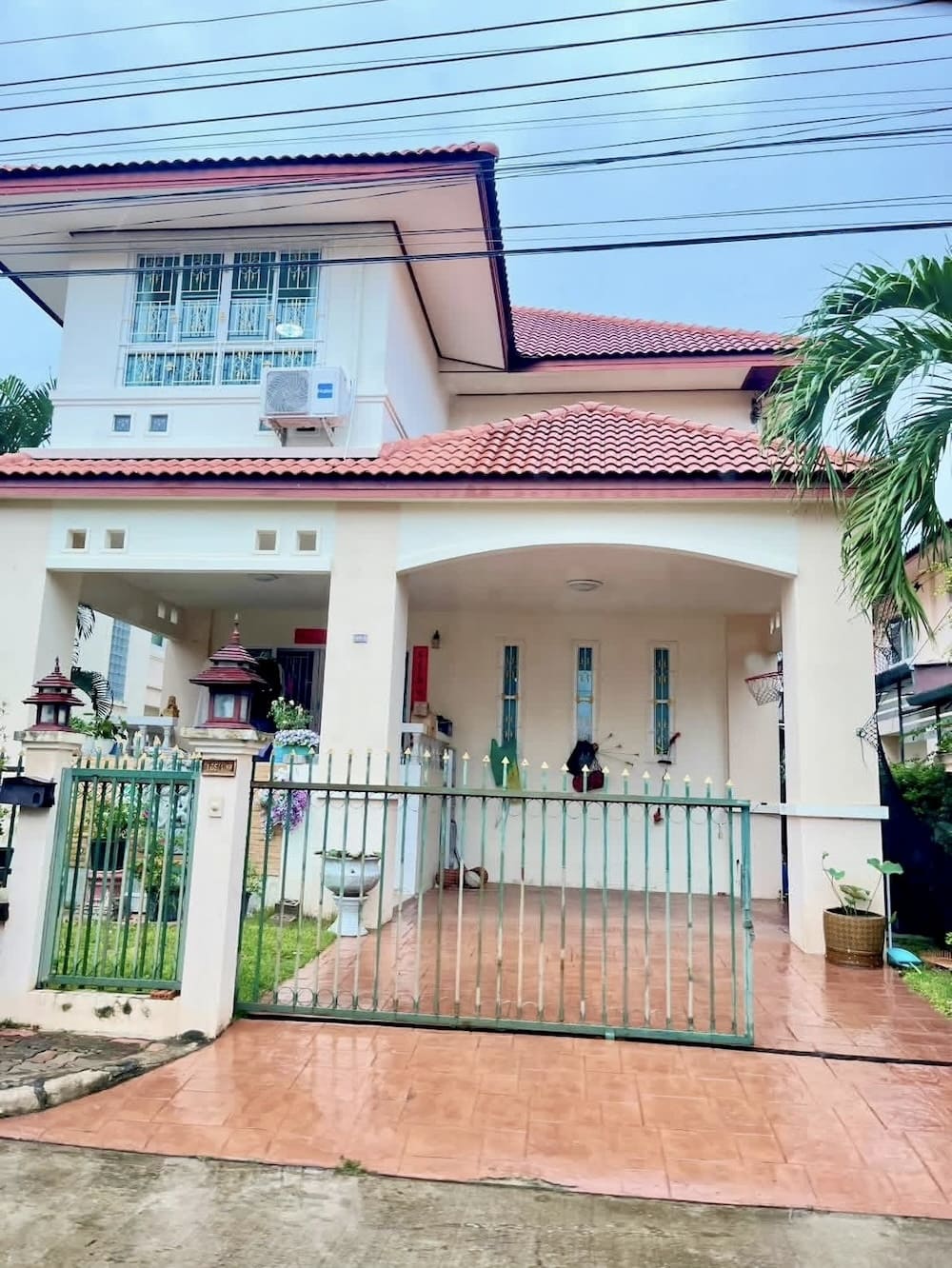 Two-story cream house with red tile roof, gated pink-tiled front yard, and potted plants near the entrance.