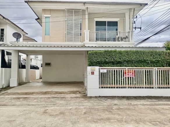 Two-story beige house with white railing, gated front yard, and a left carport; a For Rent sign on the gate.