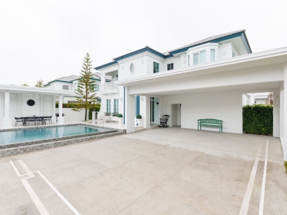 Modern white two-story house with a rectangular pool and covered patio area in a gated community.