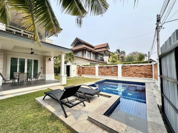 Backyard pool area with blue-tiled pool, white patio, and two black lounge chairs facing the water.