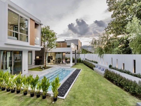 Modern two-story house with a rectangular pool, green lawn, and landscaped planter beds in a fenced backyard.