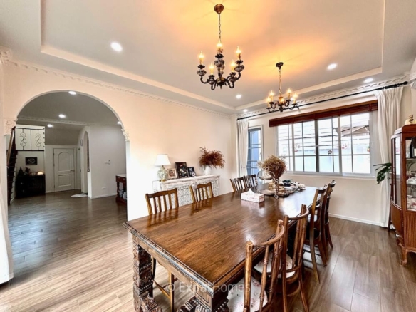 Elegant dining room with a long wooden table, chandelier lighting, and arched doorway to a hall; windowed wall with white curtains on the right.