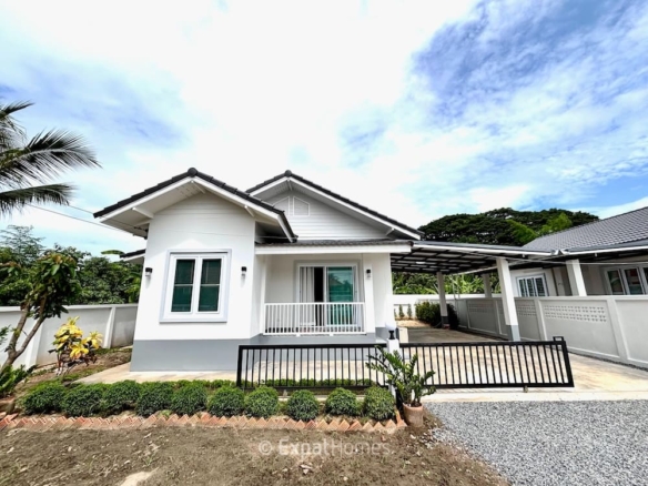 White single-story house with a small front porch, gray foundation, and a black metal fence in a manicured yard.