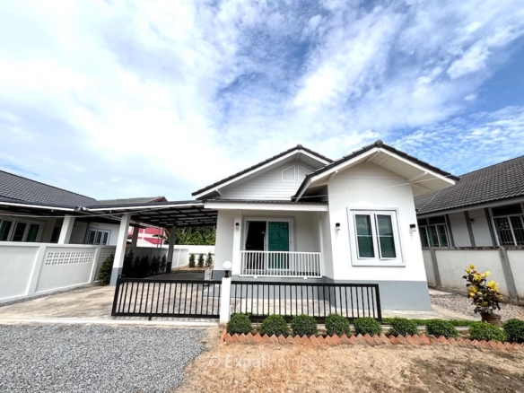 White single-story house with a small front porch, gray roof, and black metal gate under a bright sky.