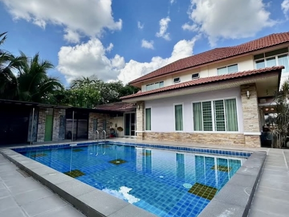 Modern two-story house with a rectangular blue pool in the backyard; red-tiled roof, stone accents, and palm trees nearby.