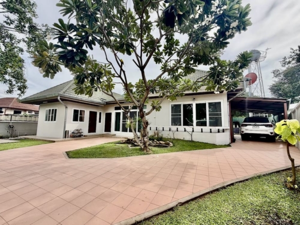 Single-story house with a tiled driveway, a large tree in the front yard, and a white SUV parked under a carport to the right.