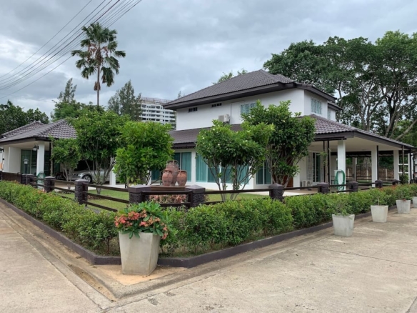 Two-story modern house with a brown tiled roof, white walls, and a fenced, manicured yard with trees and potted plants.